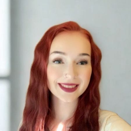 caitlin Smiling woman with long, wavy red hair and light skin, posing confidently in front of a plain light background for Ceemi Agency.
