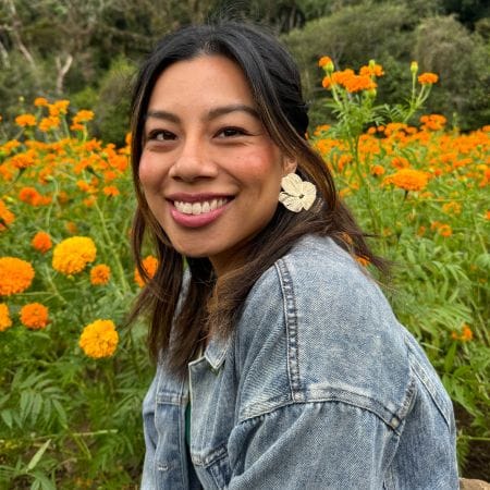 matsa Woman in a denim jacket, smiling while sitting in a field of blooming orange flowers, captures the vibrant spirit of Ceemi Agency.